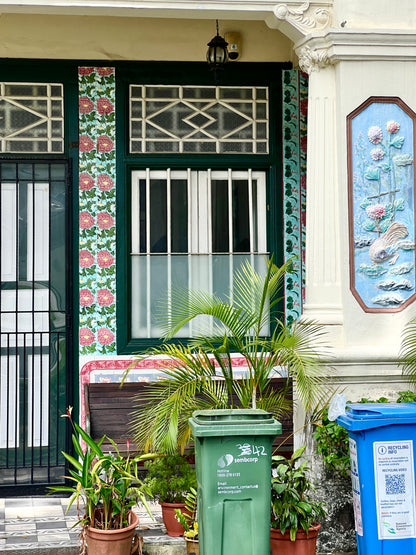 Decorative entrance with floral patterns, green and blue trash bins, and potted plants.